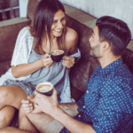 Ein Mann flirtet in einem Café in Ulm mit einer attraktiven Frau. Beide sitzen entspannt auf einer Couch und lachen miteinander beim Date.