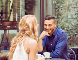 Mann und Frau beim ersten Date in einem Café, beide lächeln und lehnen sich leicht zueinander – positive Körpersprache beim Dating.