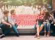 Junge Männer und Frauen sitzen lachend am Brunnen – Symbolbild für Flirtkurs Zürich.