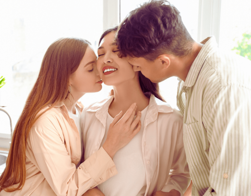 Frau wird gleichzeitig von einem Mann und einer Frau geküsst – Symbolbild für einen F-M-F-Dreier.
