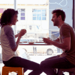 Mann und Frau sitzen in einem Café am Fenster, trinken Kaffee und führen ein lebendiges Gespräch mit sichtbarer positiver Stimmung auf dem Instant-Date.