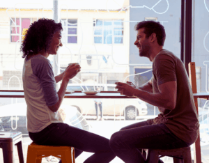 Mann und Frau sitzen in einem Café am Fenster, trinken Kaffee und führen ein lebendiges Gespräch mit sichtbarer positiver Stimmung auf dem Instant-Date.